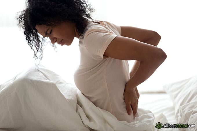 Best CBD oil for fibromyalgia: a woman sitting on a bed with lower back pain.
